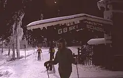 Skiers standing on snow near a balcony.