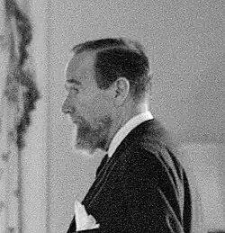 black and white head shot of a middle-aged white man with beard in checked shirt facing left.