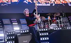 The members of Green Day performing, with frontman Billie Joe Armstrong lifting an electric guitar in the air while playing it, and drummer Tré Cool playing in the background