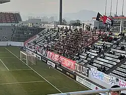 Fans of the football club Gyeongnam FC cheer for their team from a safe standing zone overlooking a football pitch from behind one of the goals.