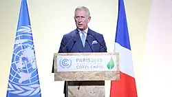 Charles delivers a speech at a podium with the French and United Nations flags behind him