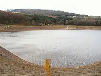 A reservoir at low volume showing stones on the surrounds, with trees in the distance