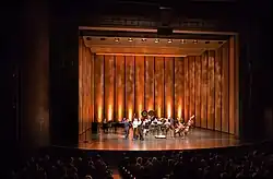 The lighted stage of a theatrical production, seen from the left side of the audience in a dark theater