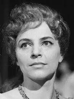 Black and white onstage publicity shot of a half-smiling young woman in stage makeup, and long, wavy hair tied back.