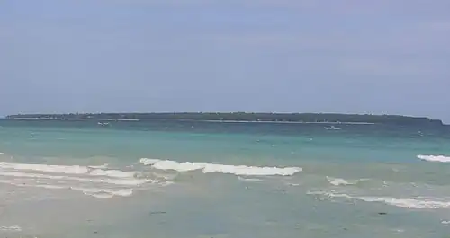 Long low green island, about 3.9&nbsp;km (2&nbsp;mi) distant. Two beaches can be made out.