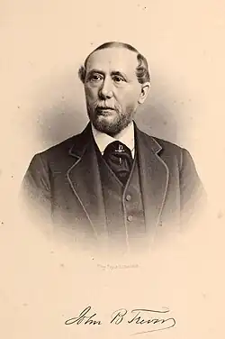 A black and white image of a man with a slight beard and mustache wearing a suit with vest, shown from the chest up