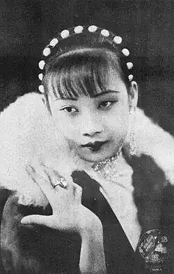 A monochrome image of a woman in jewellery and a boa, with her hand on her shoulder