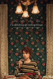 A young woman sits at a dinner table holding a drink. The background features a wallpaper decorated with flowers. Near the top of the poster are three ceiling lamps and the title, "i'm thinking of ending things".