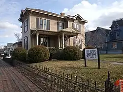 Large brown two story wooden house with sign in yard reading "Illinois Policy"