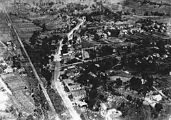 Black and white aerial photograph of Industrial City. There is a road running through the middle of the settlement and a railway line on the left side.
