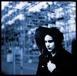 Jack White, wearing a raincoat, stares at the ground while a vulture rests on his shoulder