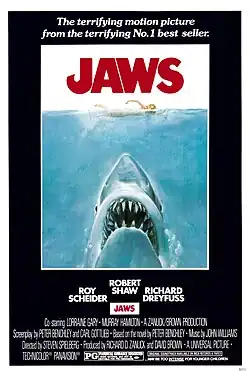 Movie poster shows a woman in the ocean swimming to the right. Below her is a large shark, and only its head and open mouth with teeth can be seen. Within the image is the film's title and above it in a surrounding black background is the phrase "The most terrifying motion picture from the terrifying No. 1 best seller." The bottom of the image details the starring actors and lists credits and the MPAA rating.
