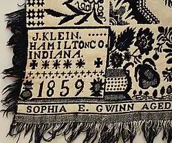 Dark blue and white, double jacquard coverlet with self fringe approx. 2.25" on two sides and bottom. Top is hemmed. Two trade blocks reading "J. Klein / Hamilton Co. / Indiana / 1859''. Woven below is "Sophia E. Gwinn Aged 16". Floral baskets border on three sides. Side borders have two rows of stars below the baskets. Field has floral medallions and eight pointed stars