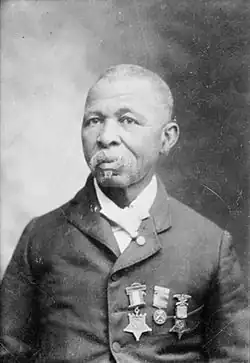 Head and shoulders of an older black man with short hair and a mustache, wearing a suit coat with three medals hanging from ribbons on the left breast.