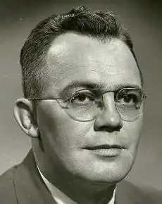 Black and white image of middle-aged man wearing glasses, a dress shirt, and suit jacket