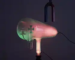 When the magnet is reversed, it bends the rays down, so the green spot is lower. The pink glow is caused by cathode rays striking residual gas atoms in the tube.