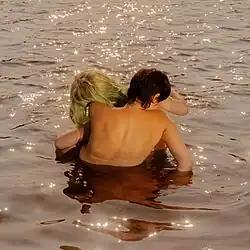 Two nude persons embracing, standing in water