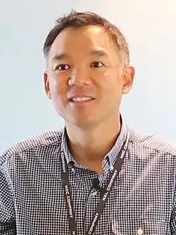 Portrait photograph of Kim smiling, while wearing a black lanyard.