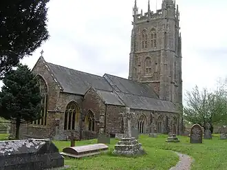 Gray stone building with ornate square tower and slate roof. In the foreground are gravestones