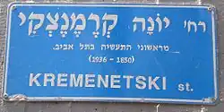 The blue Israeli street sign is in Hebrew. Translated to English it says: "Yonah Kremenetski, one of the first industrialists in Tel Aviv (1850–1936)."