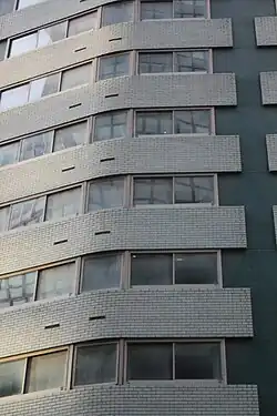 Detail of the facade, which contains a color palette of dark-green mosaic tile and turquoise brick, interspersed with windows