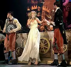 Swift singing while wearing a white dress and barefoot, holding hands with a male dancer