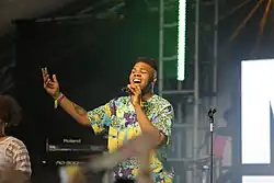 MNEK performing on a stage wearing a multi-coloured shirt.