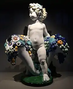 Secessionist putto with two cornucopias with floral cascades, very similar to the ones found in a lot of Art Deco of the 1910s and 1920s, by Michael Powolny, designed in c. 1907, produced in 1912, ceramic, Kunstgewerbemuseum Berlin[235]