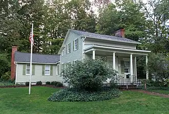 Photograph of a green house with white porch pillars and a center door with a window on either side