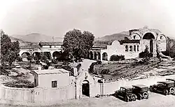 This 1921 view of the Mission San Juan Capistrano complex documents the restoration work that was already well underway by that time. The perimeter garden wall (including the ornate entranceway) and adjacent outbuilding are 1917 additions.