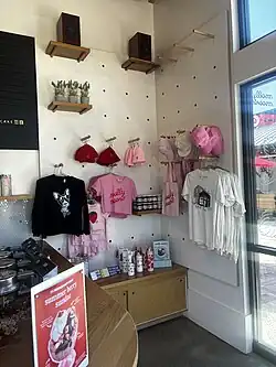 A corner of a building, white wooden walls; there are pegs on the wall that hold shirts, hats, beanies, tote bags, and water bottles with the Molly Moon's branding: either a strawberry or a dog licking an ice cream cone. Some items have the words "Molly Moon's" on them