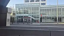 Photo of a glass station building with an entryway at ground level. An elevator and staircase are visible inside.