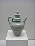 A green-tinted grey teapot with a small base and a tall body in the shape of a cone with the smallest point facing downwards. The cap covering the point that the water is poured into is a tall cylinder, and fits into a thick, wide cylindrical rim in the pot.