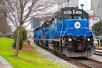 Two blue locomotives of New Orleans Belt Railway on track next to park, in front of New Orleans office buildings