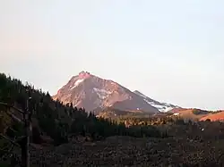 The highly eroded North Sister volcano sits above a forested area, with some ice and snow visible scattered across the mountain.