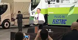 A smiling Barack Obama at a podium in front of an electric truck