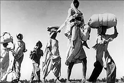 An elderly Sikh man is carrying his wife. Over 10 million people were uprooted from their homeland and traveled on foot, bullock carts and trains to their promised new home.