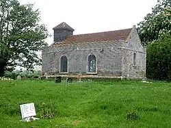 A small simple rectangular brick church seen from the southeast with two round-headed windows on the south side and a bellcote on the west gable
