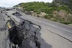 The remains of an asphalt road that has been destroyed with several pieces lifted up from the ground and others with large cracks.