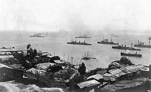 A group of large warships steaming slowly off a city.