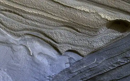 Image 11 Climate of Mars Photograph credit: NASA&nbsp;/ JPL–Caltech&nbsp;/ University of Arizona Although Mars is smaller than the Earth and 50&nbsp;percent farther from the Sun, its climate has important similarities with the Earth, such as the presence of polar ice caps, seasonal changes and observable weather patterns. This image shows layered deposits in Planum Boreum, in the north polar region of Mars, which formed from a 3-kilometre-thick (2&nbsp;mi) stack of dusty water-ice layers about 1,000&nbsp;km (600&nbsp;mi) across. The layers record information about the climate of the planet stretching back several million years. Erosion has created scarps and troughs that expose the layering. The tan-colored layers are the dusty water ice of the polar layered deposits, however a section of bluish layers is visible below them. These bluish layers contain sand-sized rock fragments that likely formed a large polar dunefield before the overlying dusty ice was deposited. This photograph, depicting an area approximately 1.3&nbsp;km (0.8&nbsp;mi) across, was captured by the HiRISE camera on board NASA's Mars Reconnaissance Orbiter. More selected pictures