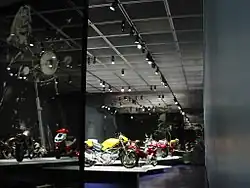 Translucent panel reaching floor to ceiling, with image of voluptuous blond woman on a motorcycle in front of chamber with several motorcycles on pedestals.