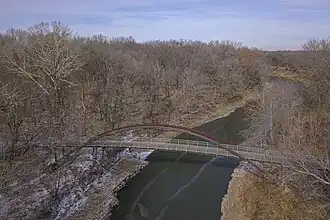An aerial image of the Pathfinder Parkway bridge, a suspension footbridge with wooden planks, and the Candy River, with spots of snow on the ground