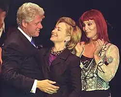 Cher standing beside President Bill Clinton and First Lady Hillary Clinton at a birthday celebration, all smiling.