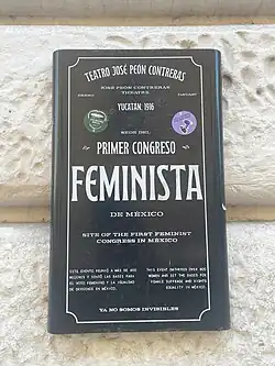 A plaque on the outside wall of the Teatro Peón Contrera. It says "Teatro José Peón Contreras, Yucatan 1916. Sede del Primer Congreso Feminista de México. Site of the First Feminist Congress in Mexico". This is followed by a small block of text describing the events of the congress. At the bottom of the plaque, it reads "Ya no somos invisibles".