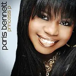 A close-up photo of Paris Bennett with long black hair, wearing a gold hoop earring and chains against a grey background. Both the artist's name and album title are placed vertically on the left side of the cover, colored in black and gold respectively.