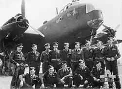 Black-and-white photo of a group of young men wearing military uniform in a formal pose in front of a larger World War II-era propeller aircraft