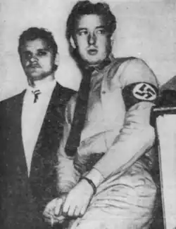 Black and white photo of Forbes wearing a Nazi armband and being led away in handcuffs