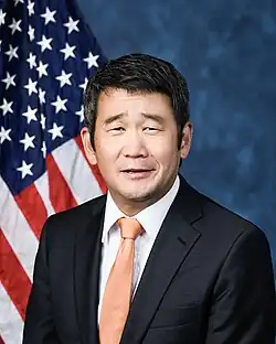 Official House portrait of Min smiling in front of the U.S. flag, wearing a black suit, white shirt, and orange tie.