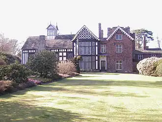 View of old country house seen across gardens; the exterior walls of the house are in Tudor black and white